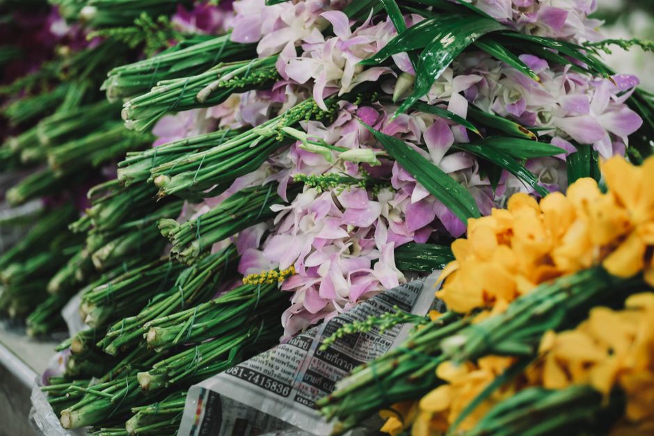 An arrangement of fresh flower stems, including lavender and yellow tulips, wrapped in newspaper and laid out on a surface, ready for floral gift or flower delivery. The lavender stems are delicate wi