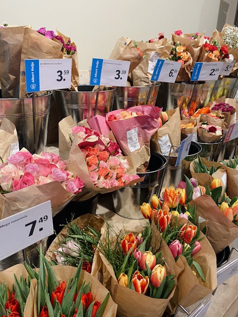 A display of various floral bouquets arranged in metal buckets at a florist shop, with prices clearly labeled on tags. The bouquets feature a range of fresh flowers, including pink roses, orange and y